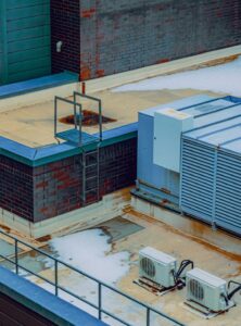 Facility staff inspect a commercial rooftop unit beside roof drains and maintenance tools.