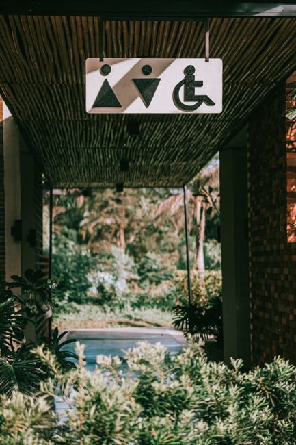 Facility staff inspect a clear wheelchair-accessible route, entrance, ramp, and restroom doorway.